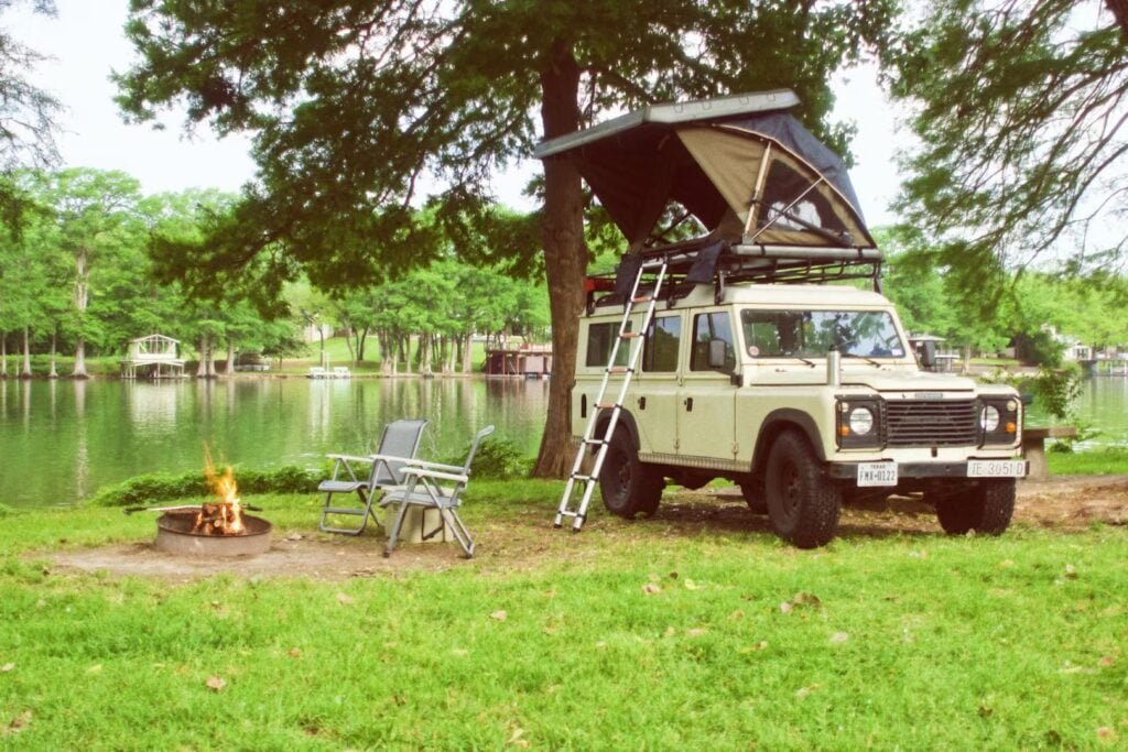A rooftop tent on a car next to a camp fire,on the grass next to a lake